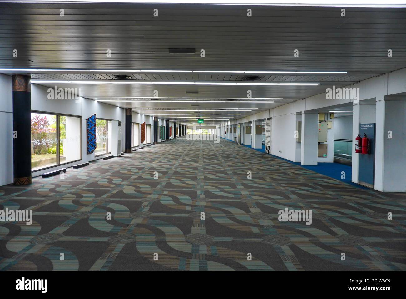 Una spaziosa passerella vuota con un tappeto a motivi geometrici conduce a una luce lontana; adatta per illustrare il design o l'architettura di un aeroporto o di un centro congressi Foto Stock