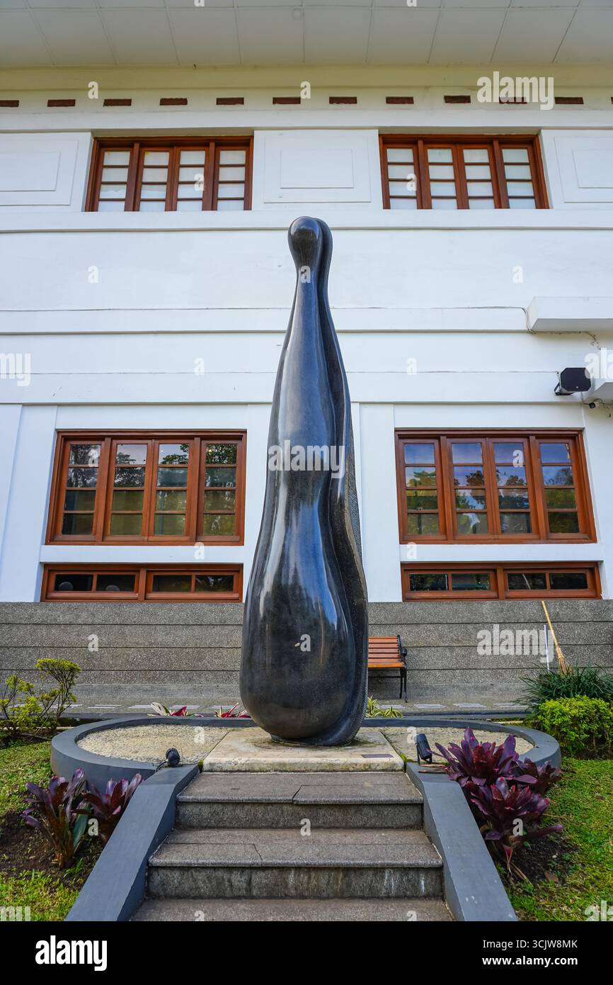 La scultura astratta nera sorge graziosamente in un parco paesaggistico contro la facciata di un edificio, creando un interesse visivo adatto all'arte e all'architettura Foto Stock