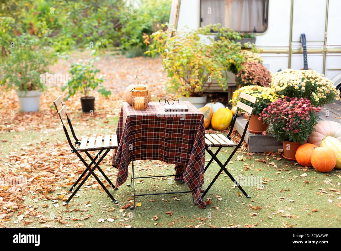 Accogliente giardino esterno autunnale - tavolo e sedia, libri, fiori, foglie cadute. Casa sul retro con mobili da giardino, decorazioni autunnali e piante e zucche. Foto Stock