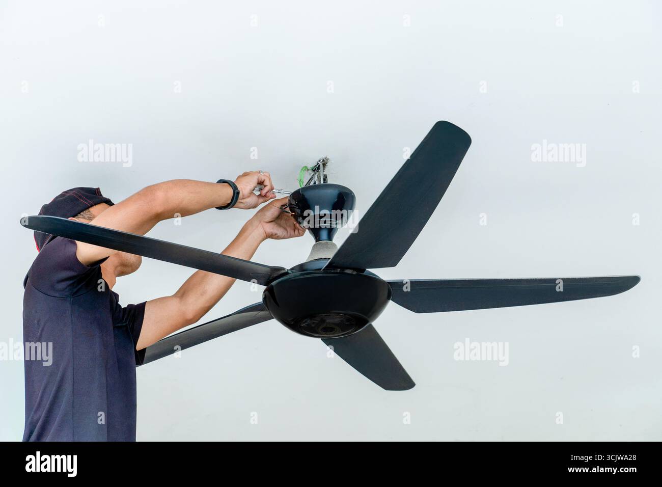 Un uomo che installa un ventilatore a soffitto. Miglioramento della casa, lavoro professionale e concetto di competenze tecniche. Foto Stock