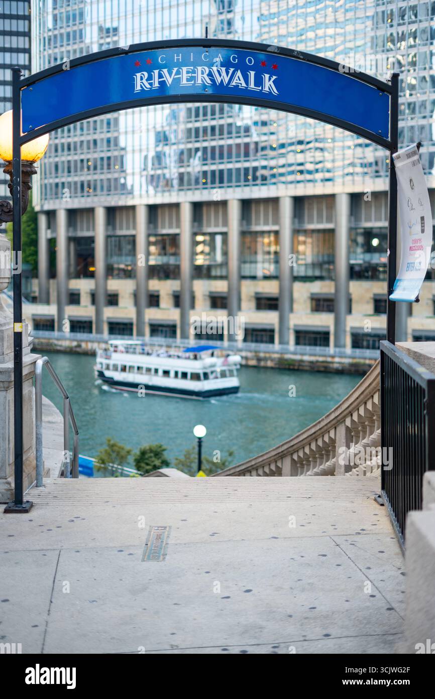 L'insegna del Chicago Riverwalk conduce verso il cuore storico della città: Il fiume luccicante, il passaggio dei traghetti e le storie urbane che ti attendono appena oltre la cornice. Foto Stock