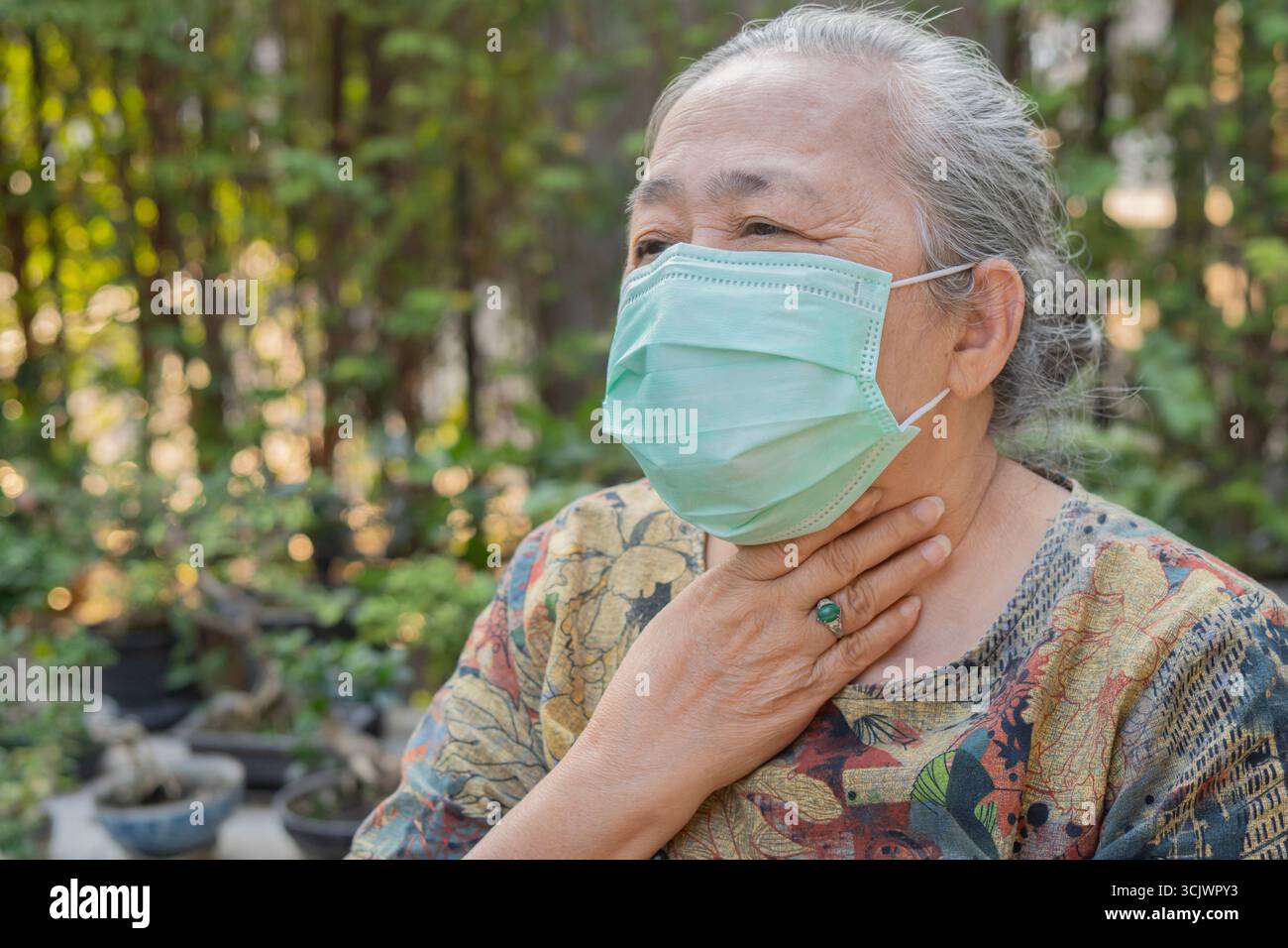 All'aperto ritratto donna anziana che indossa maschera medica monouso e mal di gola da tosse. Concetto senior di salute. Foto Stock