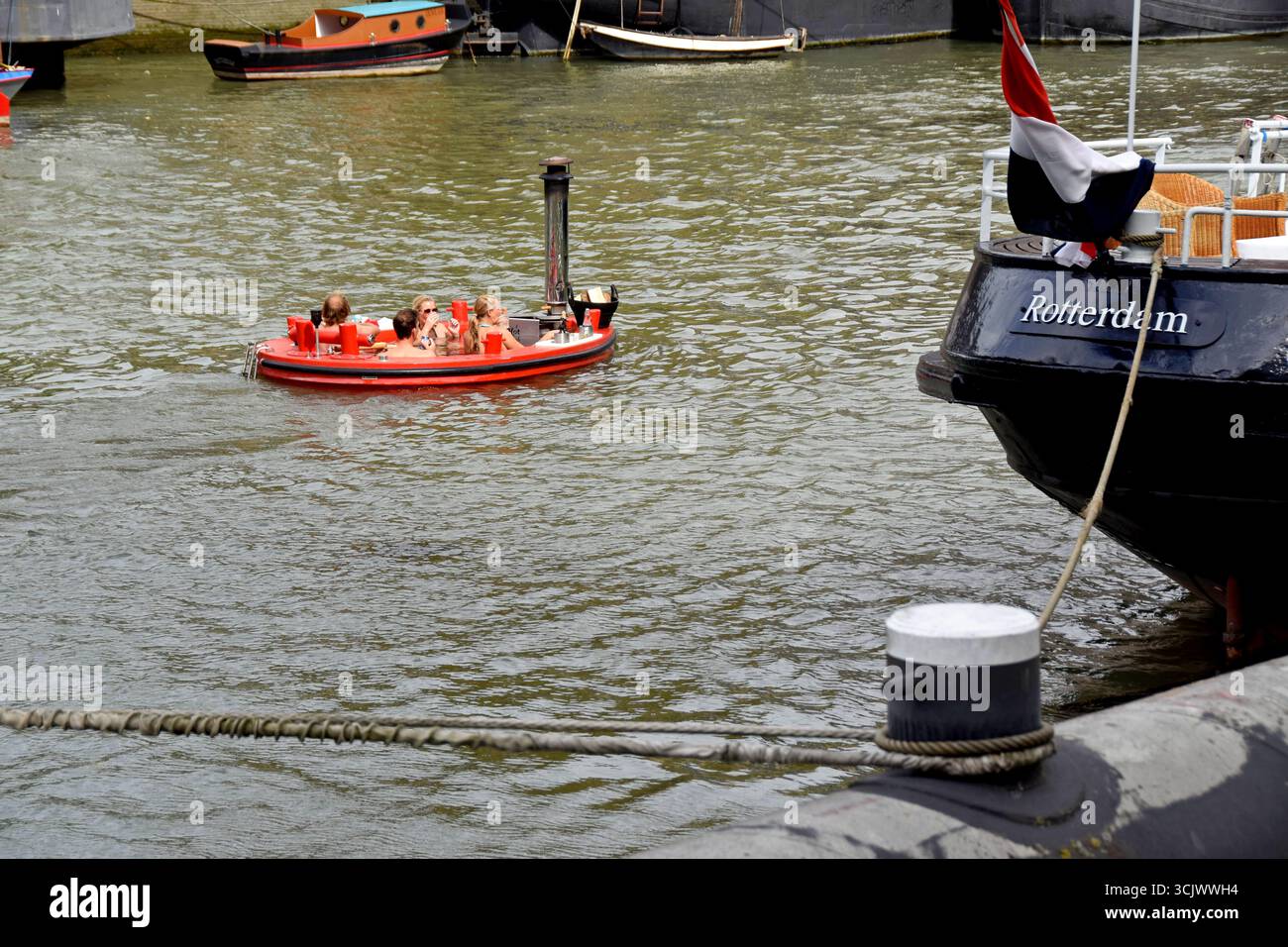 Persone in una vasca idromassaggio galleggiante a legna che attraversa il porto di Rotterdam, Paesi Bassi, agosto 2025 Foto Stock