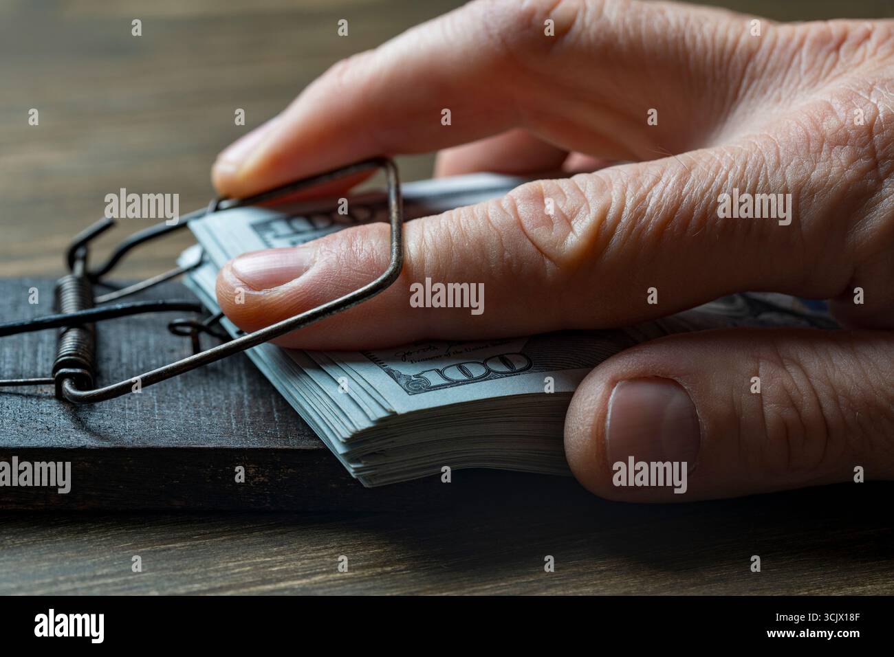 Una pila di banconote da 100 dollari in mousetrap di legno con la mano intrappolata, primo piano. Concetto di truffa o frode. Rischi e pericoli degli investimenti Foto Stock