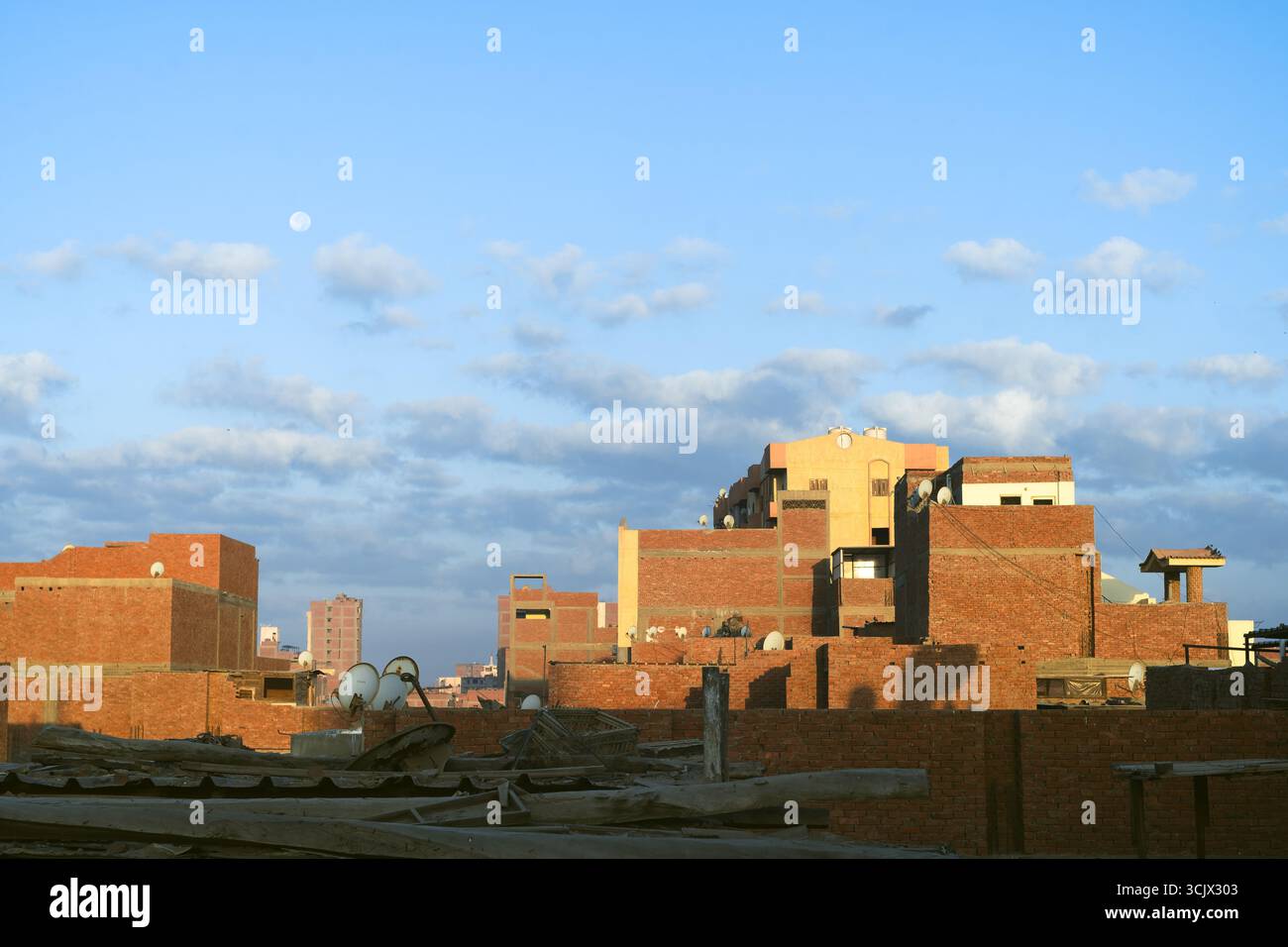 Scenario generale di luna che si innalza sull'edificio residenziale egiziano in mattoni rossi con atmosfera nuvolosa nell'autunno del 2025 Foto Stock