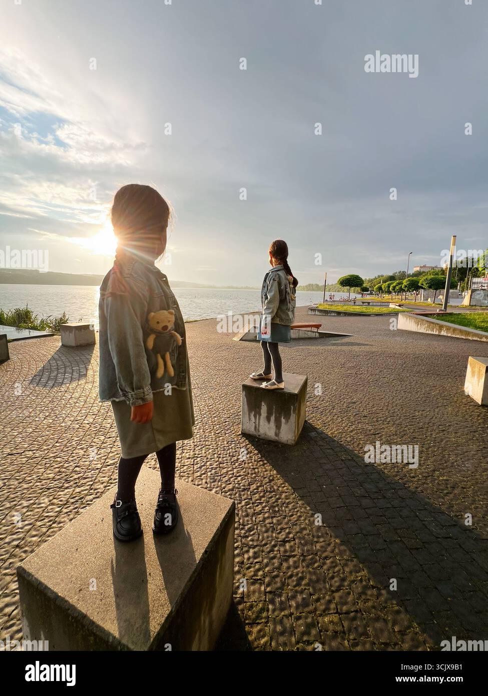 Due bambini che si godono il tramonto sul lungomare stando in piedi su piattaforme di pietra. Foto Stock