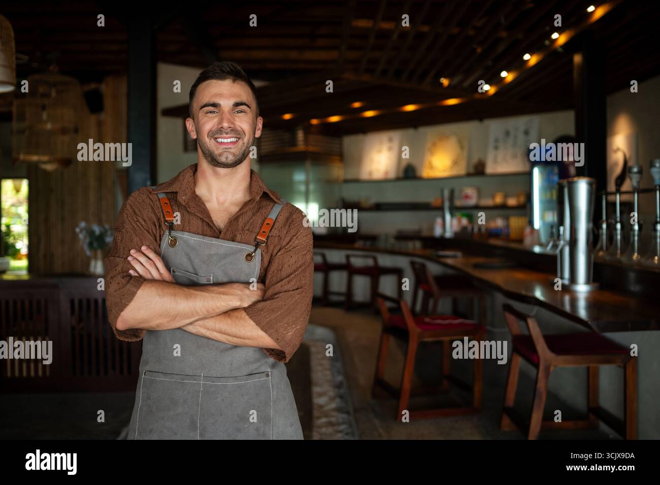 Orgoglioso proprietario di un caffè che si trova con fiducia dietro il bancone, pronto a servire i clienti con un sorriso caldo Foto Stock