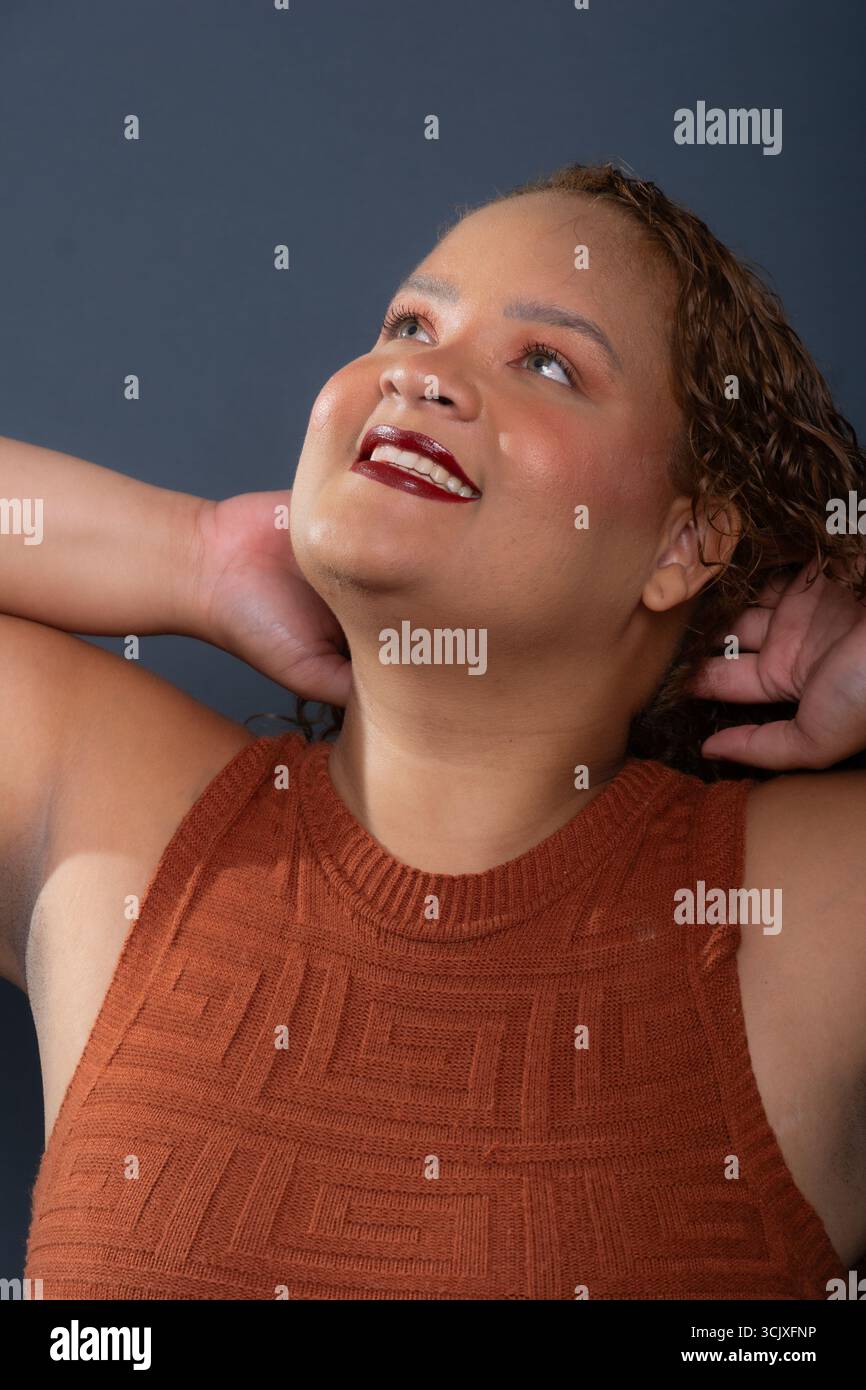 Ritratto ravvicinato di una bella donna sorridente con capelli ricci marroni che guarda la fotocamera isolata su sfondo grigio. Persona sicura di sé. Foto Stock