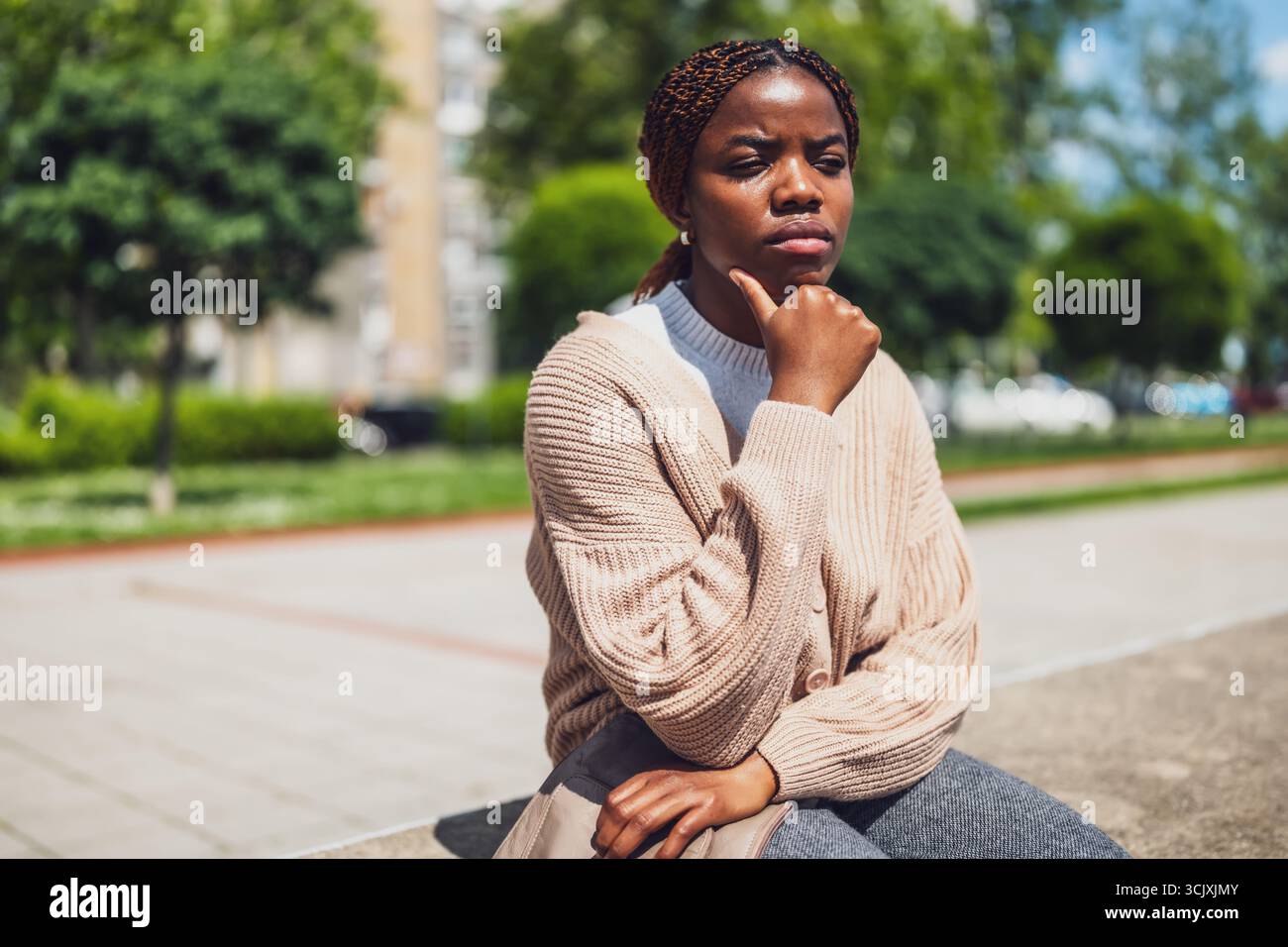 Ritratto di uno stile di vita urbano di una donna afroamericana che affronta lo stress emotivo, seduta nel parco cittadino. Foto Stock