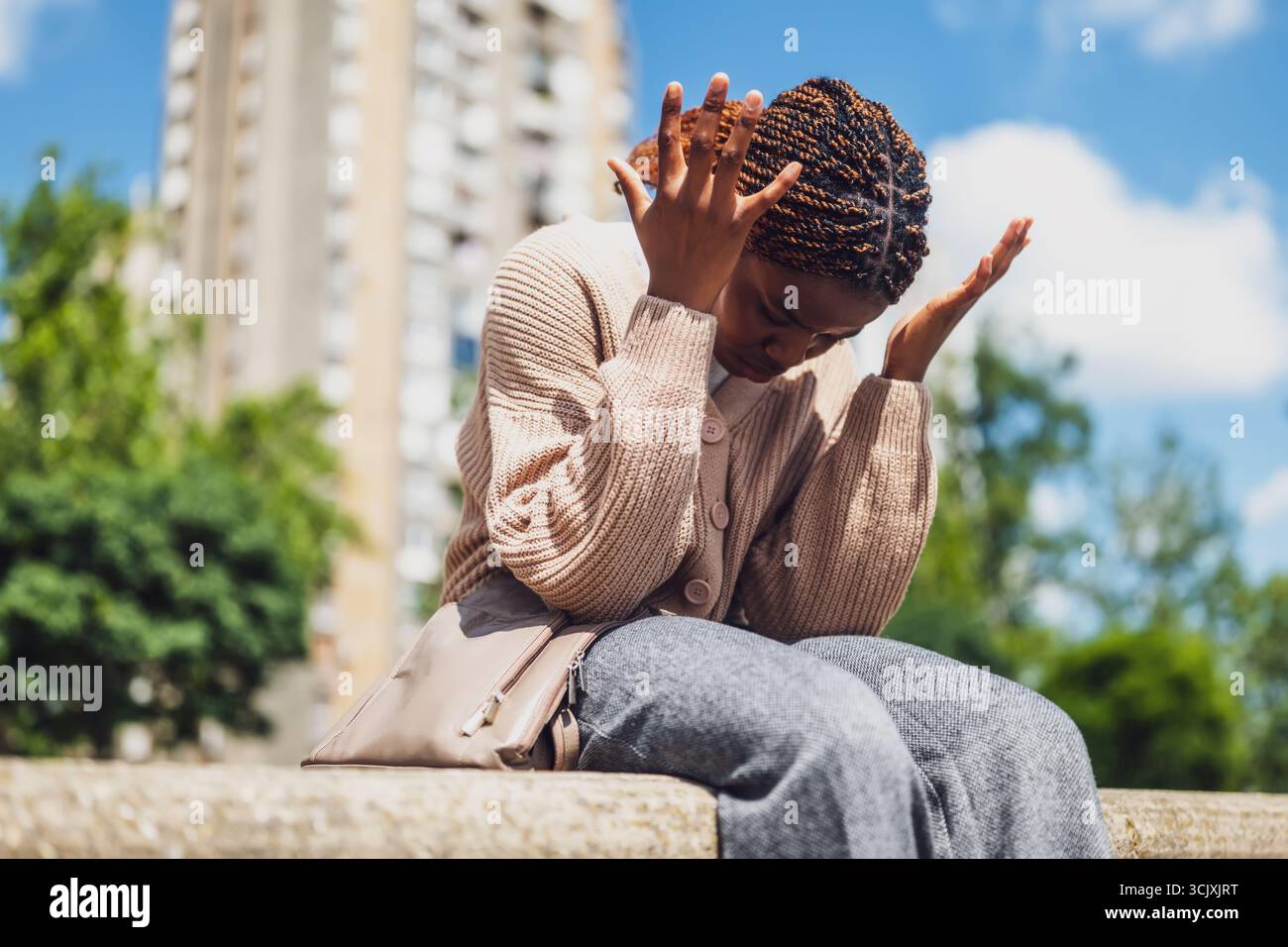 Ritratto di una giovane donna africana sconvolta seduta in un parco della città. Foto Stock