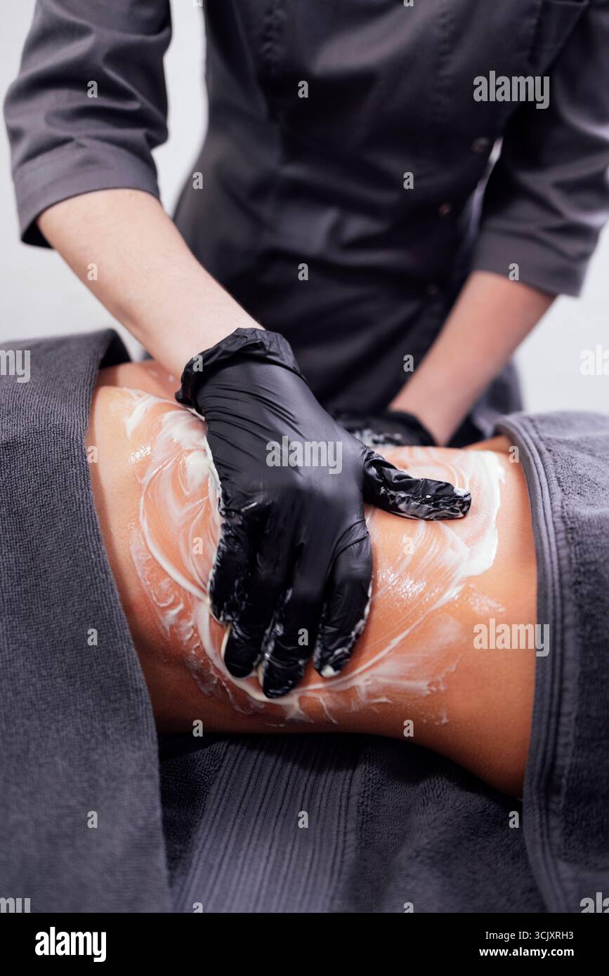 L'estetista femminile applica crema sulla pelle dei clienti, dimostrando tecniche di cura della pelle in un ambiente tranquillo spa, promuovendo il relax e il benessere Foto Stock