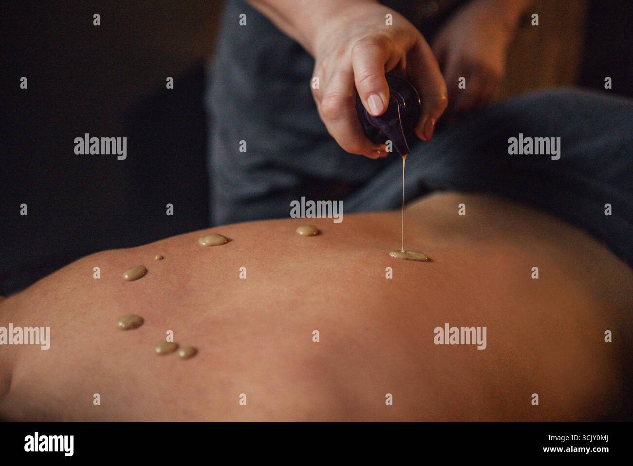 Una cliente femminile si sta godendo un massaggio rilassante con olio applicato alla schiena, evidenziando il relax e il benessere in un ambiente spa sereno con delicati Foto Stock