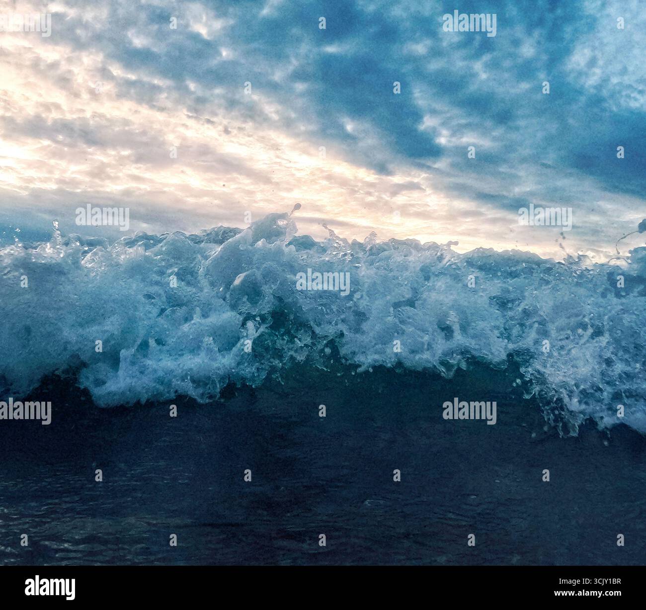 Le onde si infrangono sulla spiaggia sabbiosa, con un cielo nuvoloso sopra, mostrando l'interazione dinamica tra acqua e cielo in una tranquilla scena costiera Foto Stock