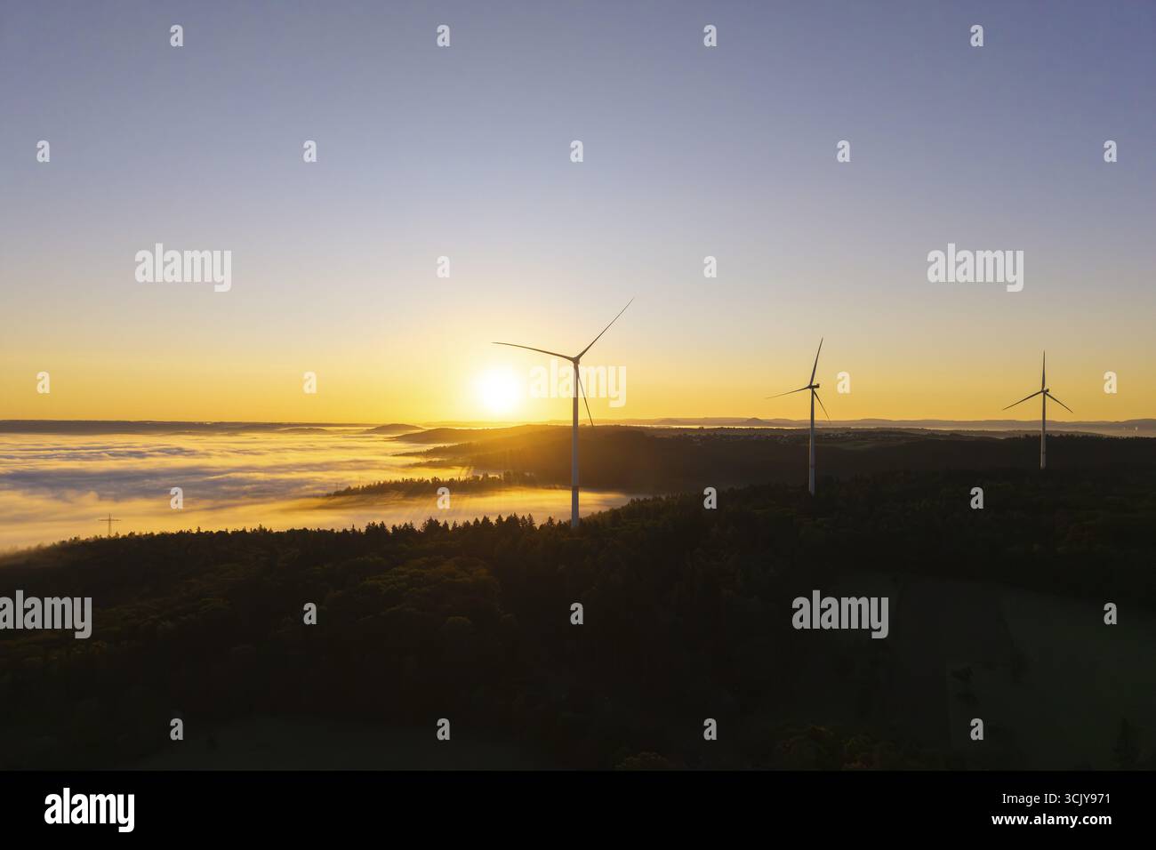 Tre turbine eoliche si affacciano su una foresta ricoperta di nebbia all'alba, vicino a Schorndorf, distretto di Rems-Murr, Rems-Murr-Kreis, Baden-Wuerttemberg, Germania Foto Stock