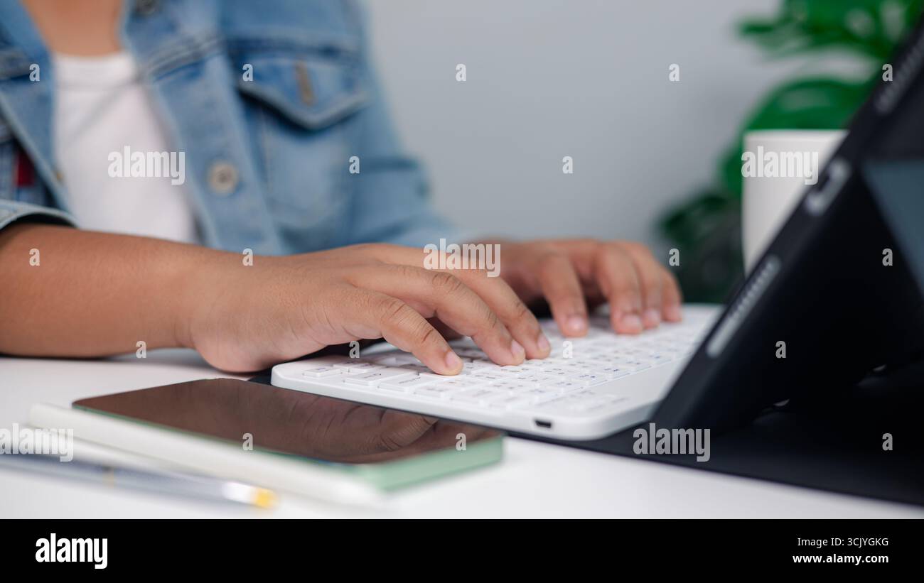 Primo piano della digitazione manuale su tastiera wireless con tablet sulla scrivania, concetto di lavoro freelance, business online, lavoro in remoto e moderno ambiente di lavoro digitale Foto Stock