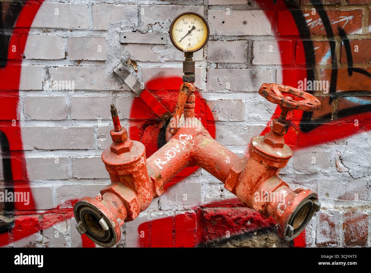 Idrante rosso sopra il suolo, Un raccordo per il prelievo dell'acqua da Un sistema di distribuzione dell'acqua e Un manometro su una parete in mattoni imbiancati Foto Stock