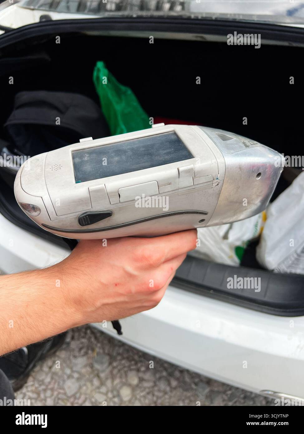 Gorodok, Ucraina - 15 agosto 2025: Presa manuale di un dispositivo tecnologico del convertitore catalitico portatile analizzatore XRF con involucro in argento vicino a un veicolo t Foto Stock