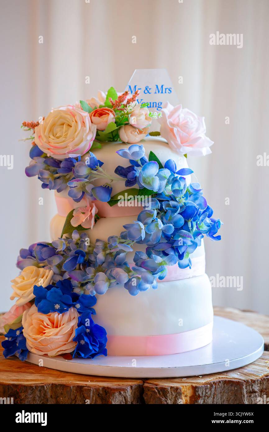 Elegante torta nuziale a tre piani decorata con una cascata di peonie artificiali e ortensie Foto Stock