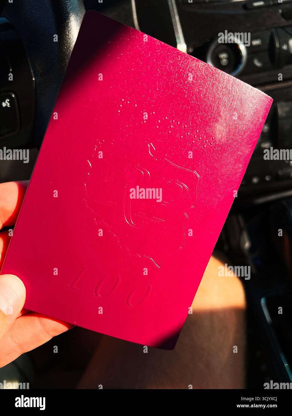 Un passaporto rosso della Polonia è tenuto da una mano all'interno di un'auto, con dettagli in rilievo. 100 anni dalla seconda Repubblica polacca Foto Stock