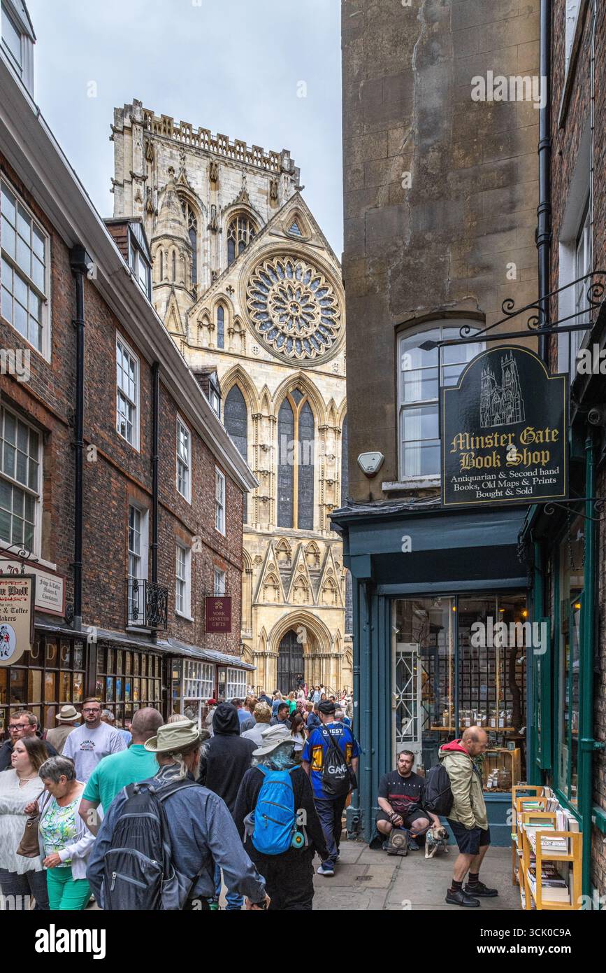 Scena di strada a York, in Inghilterra, con pedoni e negozi di fronte alla cattedrale di York Minster, tra cui il Book Shop di Minster Gate e l'architettura gotica Foto Stock
