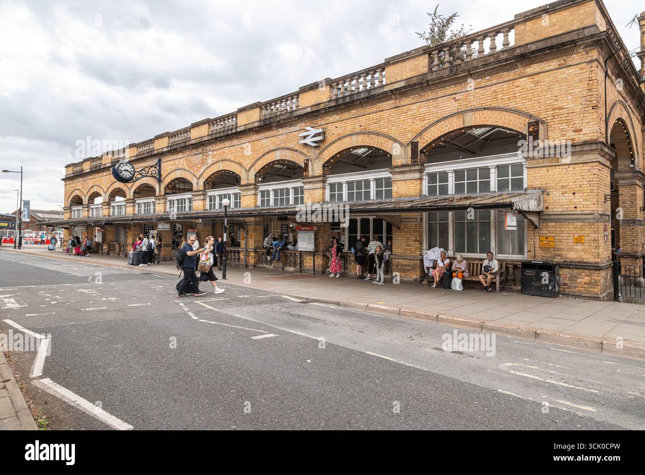 I viaggiatori si riuniscono fuori dalla stazione ferroviaria di York in Inghilterra, con bagagli, segnaletica e attività stradali che suggeriscono una giornata intensa di partenze e arrivi Foto Stock