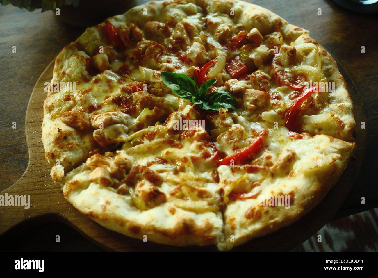 Un vassoio di pizza al formaggio di pollo con condimenti di pezzi di carne di pollo, formaggio fuso, cipolle, peperoni e un contorno di una foglia di basilico Foto Stock