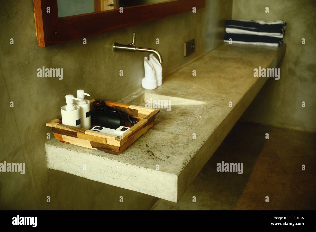 Un'area lavandino industriale del bagno, con un ripiano in cemento, un rubinetto a parete, prodotti da bagno e asciugamani Foto Stock