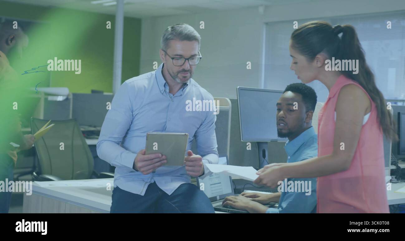 Uomo in tuta che tiene un tablet e conduce discussioni in un ufficio open space, con monitor e documenti Foto Stock