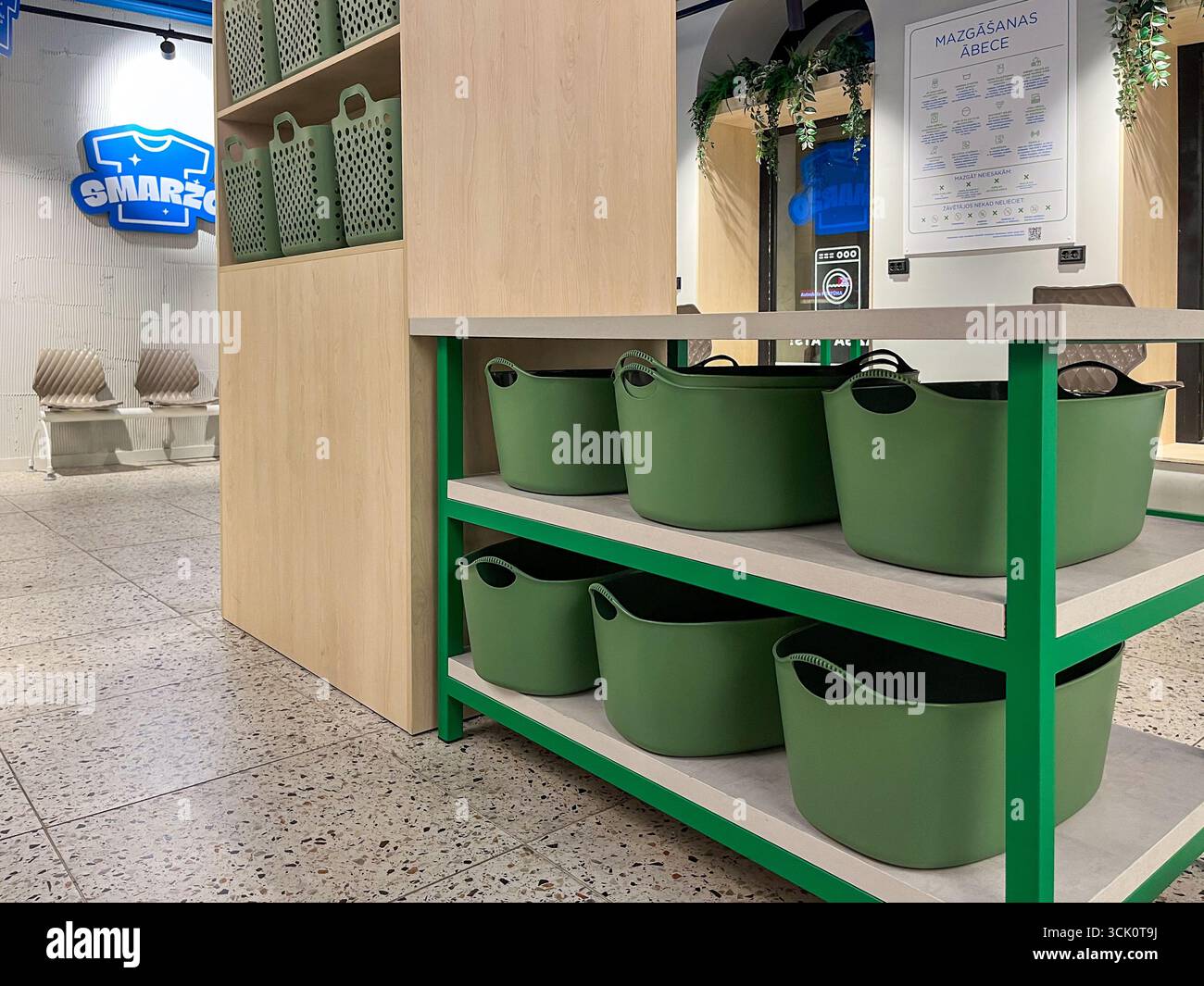 Riga, Lettonia - 4 settembre 2025: Moderna lavanderia con cesti verdi sugli scaffali, per migliorare l'esperienza self-service in un ambiente luminoso e accogliente Foto Stock