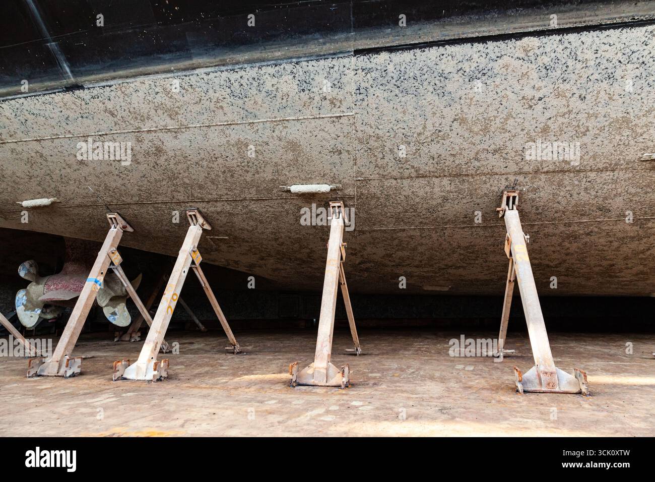 La parte poppa di un grande yacht a motore con eliche azimutali è ancorata a secco su blocchi di legno e sostenuta da supporti metallici. Foto Stock