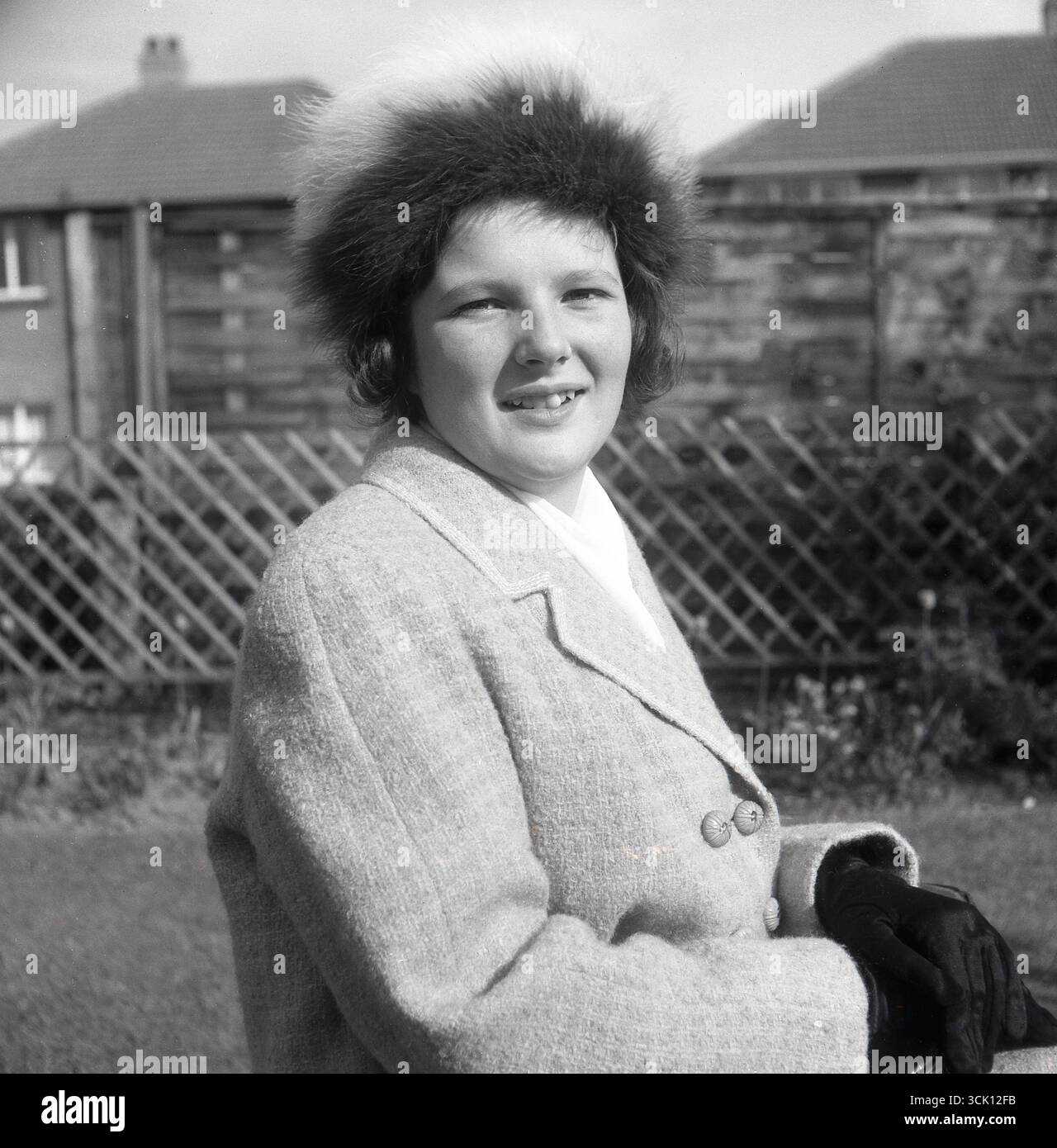 Anni '1960, storica, all'aperto in un giardino, una giovane signora, vestita con un elegante cappotto leggero, guanti e un morbido cappello soffice, un cappello in pelliccia sintetica, in posa per la sua foto, Inghilterra, Regno Unito. Foto Stock