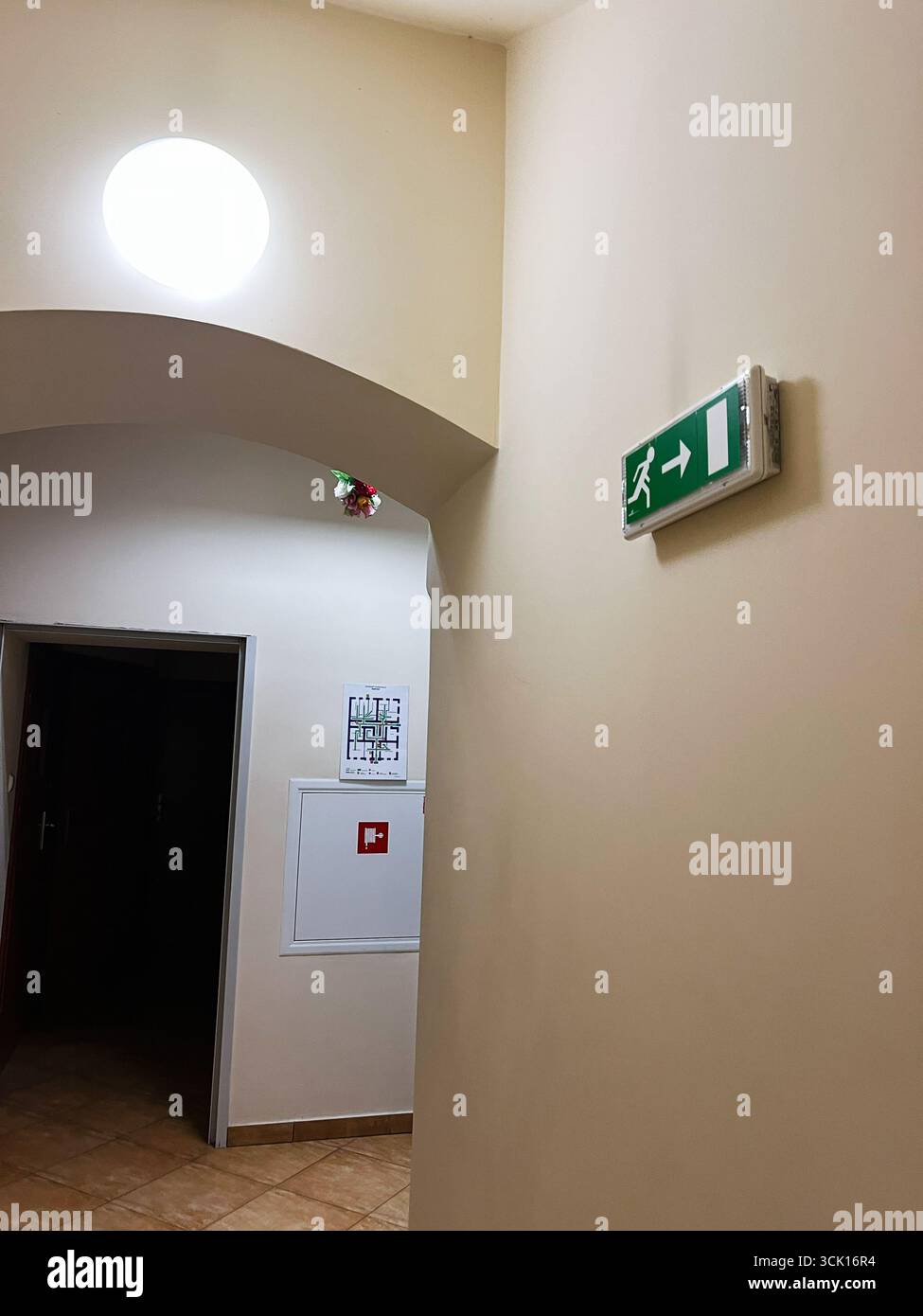 Angolo luminoso del corridoio con segnale di uscita, pavimento piastrellato e segnali di sicurezza Foto Stock