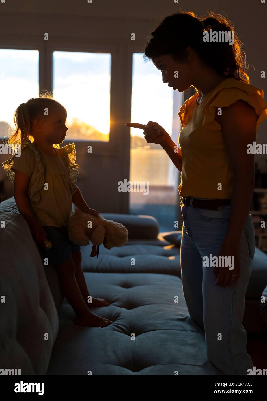 La madre sta delicatamente rimproverando sua figlia mentre si siedono in un accogliente salotto, con una calda scena illuminante al tramonto Foto Stock