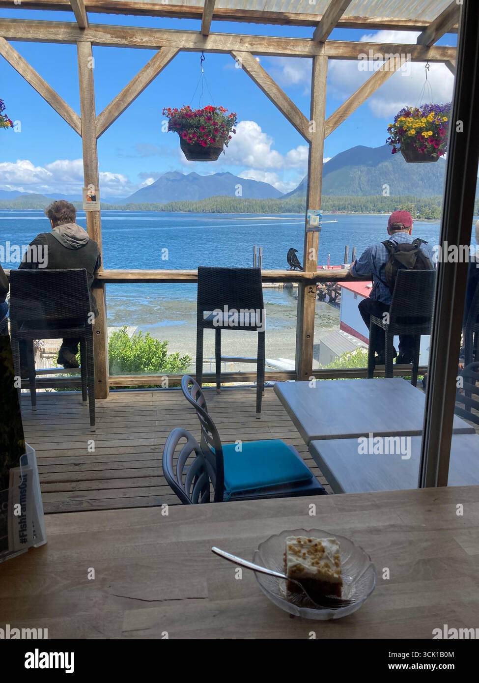 Clienti seduti sulla terrazza esterna dell’Harbourview Coffeehouse con vista sul Clayoquot Sound a Tofino, Isola di Vancouver, Columbia Britannica. - Immagine stock catturata con smartphone