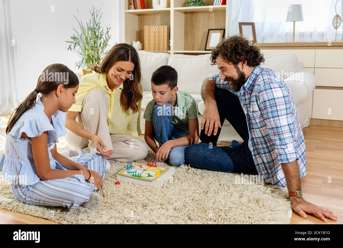 La famiglia di quattro persone si riunisce nel proprio soggiorno per una divertente serata di gioco, condividendo risate e momenti piacevoli insieme su un tappeto morbido Foto Stock