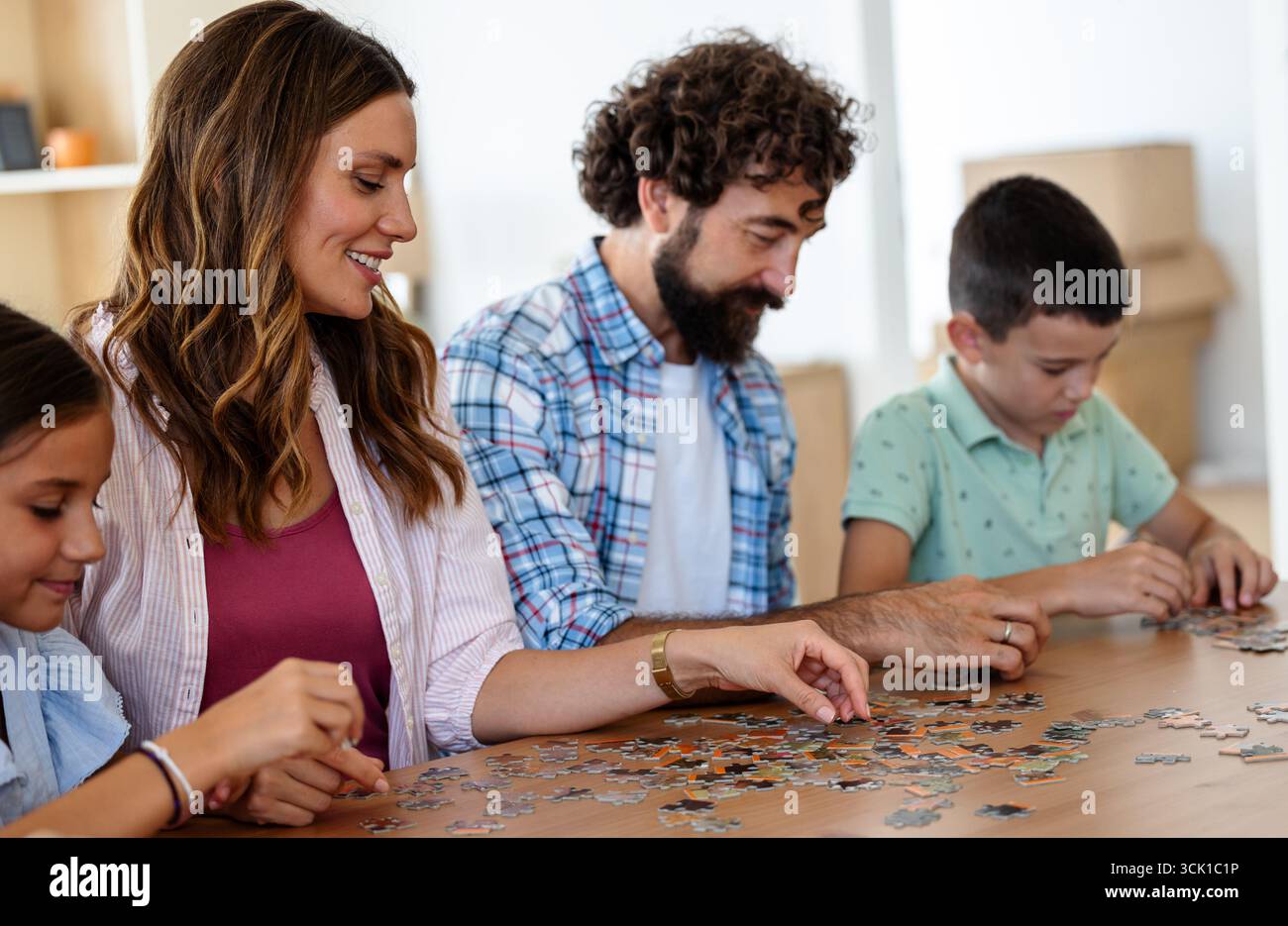 La famiglia si siede al tavolo lavorando al puzzle, godendosi momenti di qualità insieme nel soggiorno ben illuminato di casa Foto Stock
