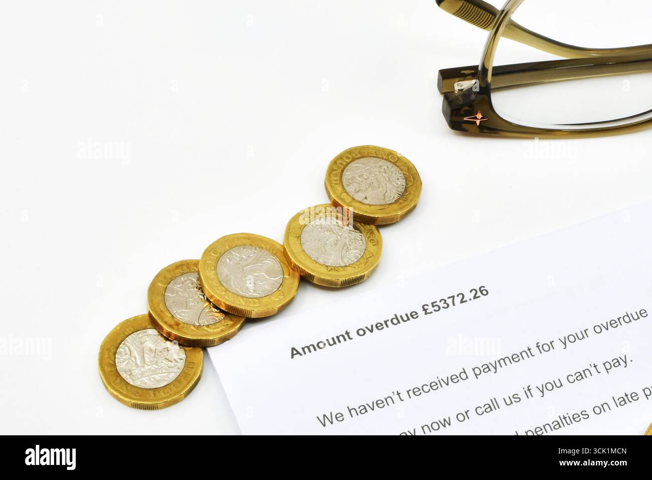Vista ravvicinata di una lettera ufficiale su una quantità di debito scaduta, con monete inglesi da una sterlina e un paio di bicchieri. Niente persone. Foto Stock