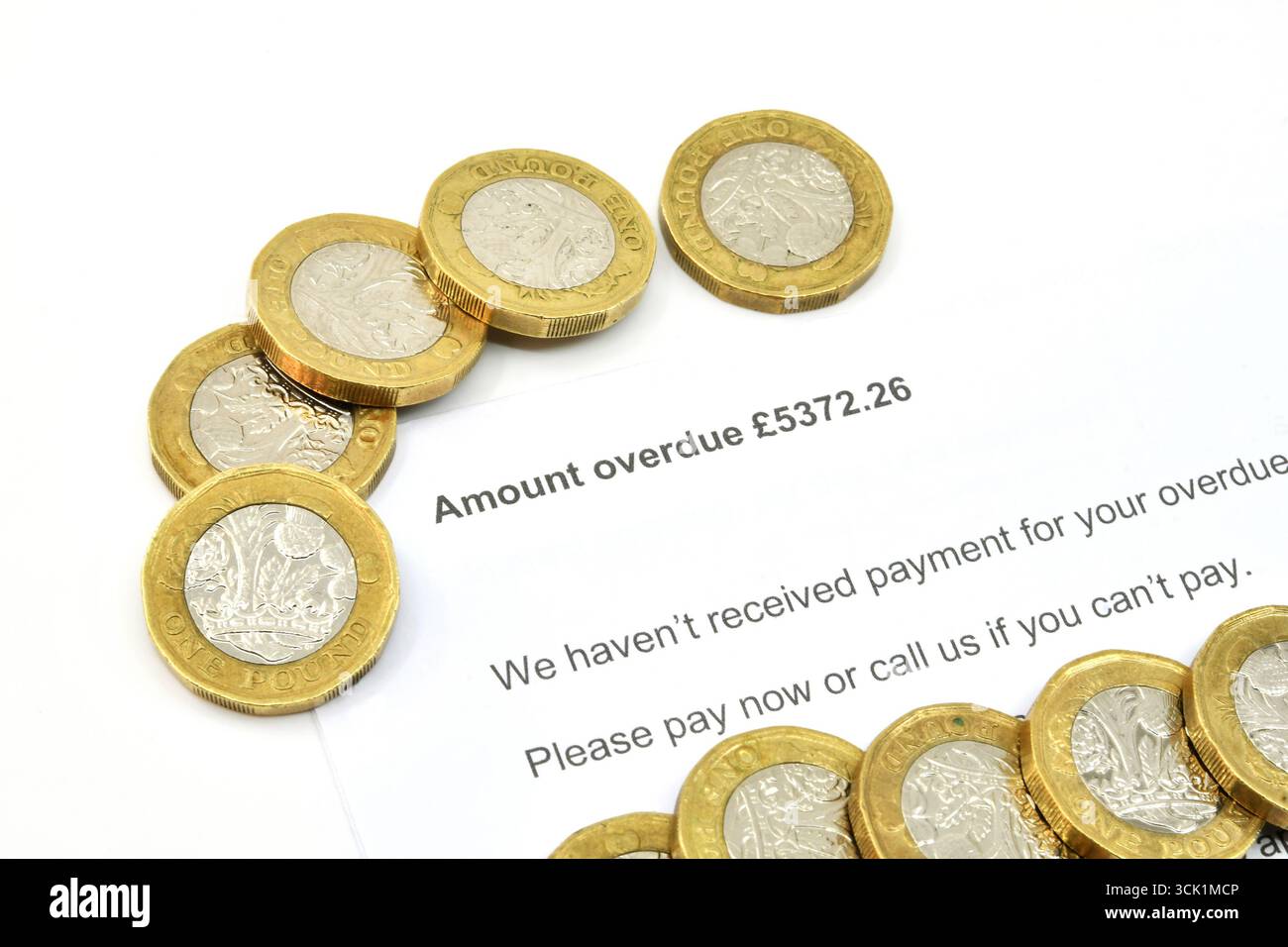Vista ravvicinata di una lettera ufficiale su una quantità di debito scaduta, con monete inglesi da una sterlina. Niente persone. Foto Stock