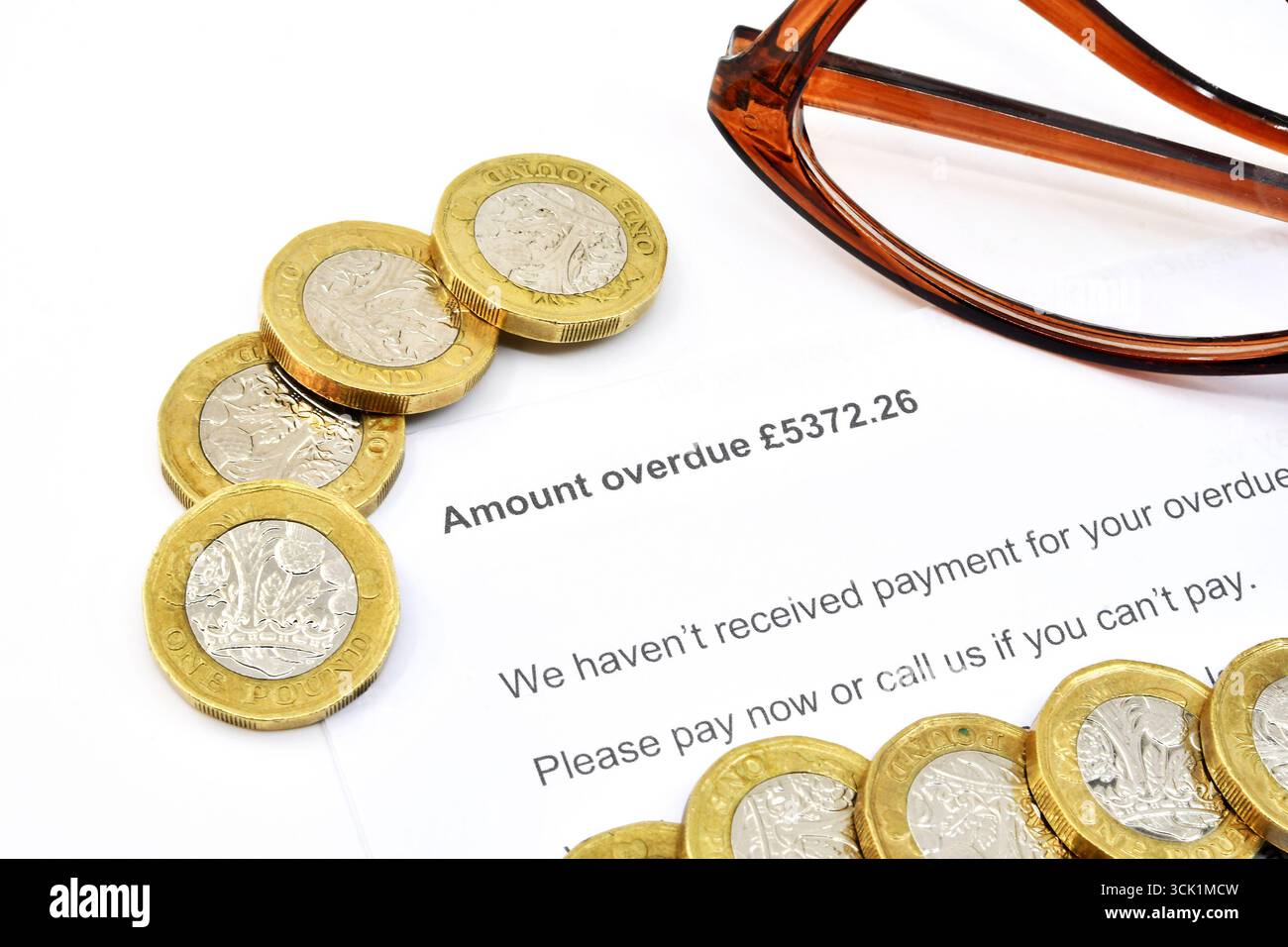 Vista ravvicinata di una lettera ufficiale su una quantità di debito scaduta, con monete inglesi da una sterlina e un paio di bicchieri. Niente persone. Foto Stock