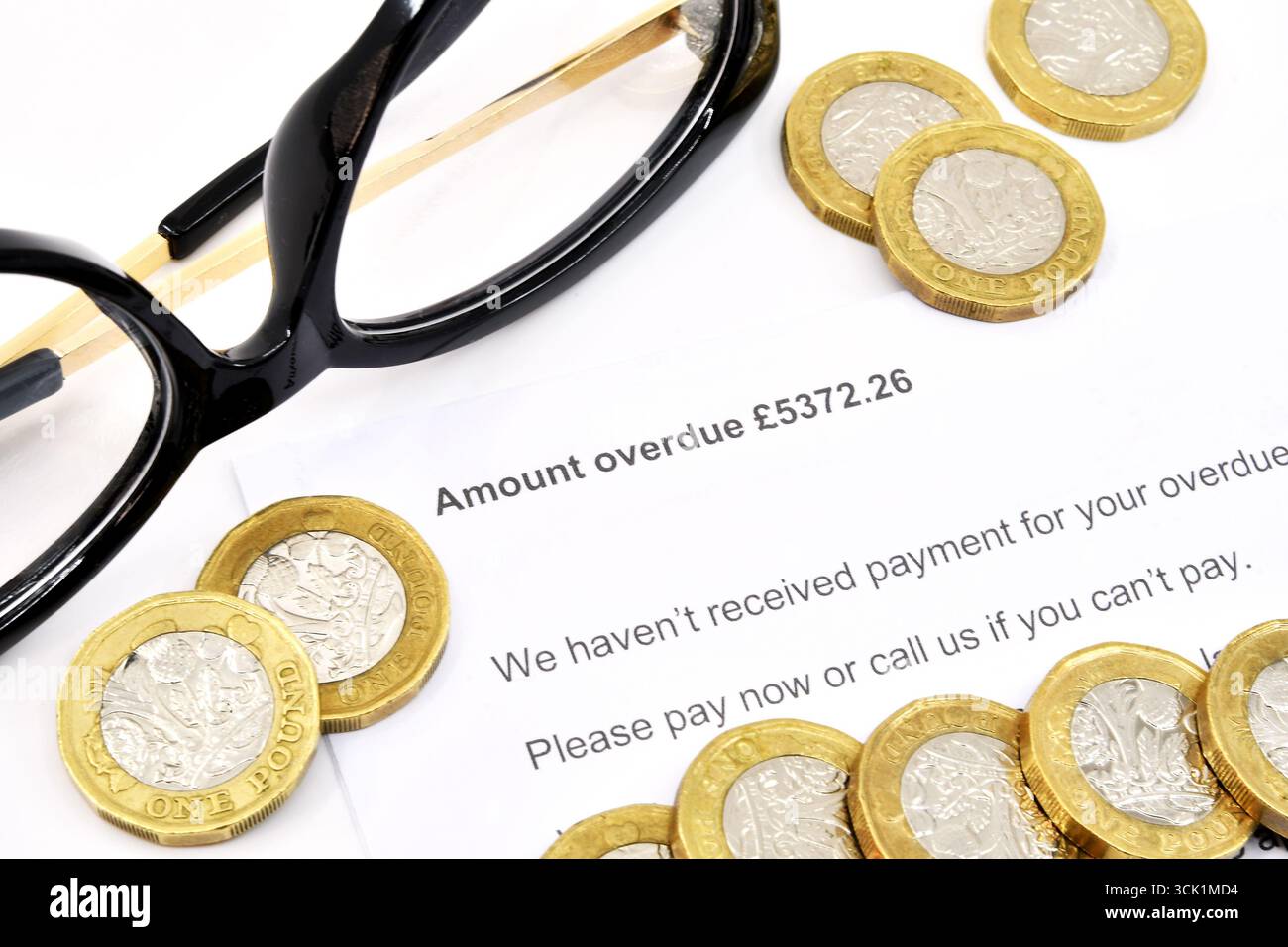 Vista ravvicinata di una lettera ufficiale su una quantità di debito scaduta, con monete inglesi da una sterlina e un paio di bicchieri. Niente persone. Foto Stock