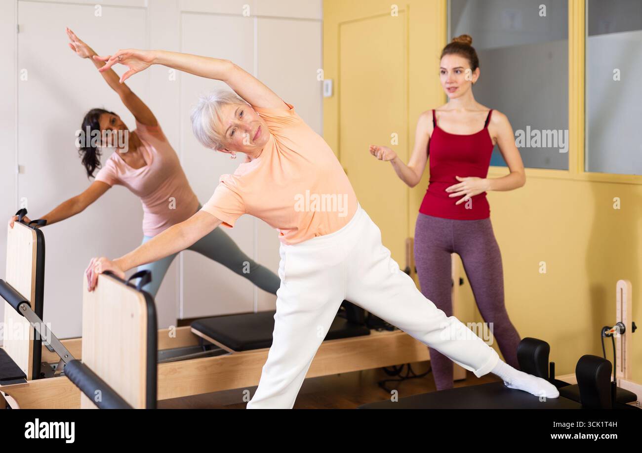 Donna anziana che esegue pilates esercizi sul riformatore durante l'allenamento di gruppo Foto Stock