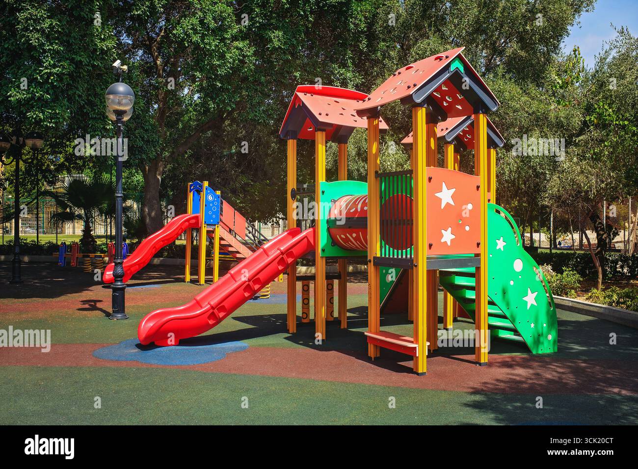 Parco giochi colorato con scivoli e strutture per giochi su soffice pavimento in gomma in un parco soleggiato tra alberi. Foto Stock