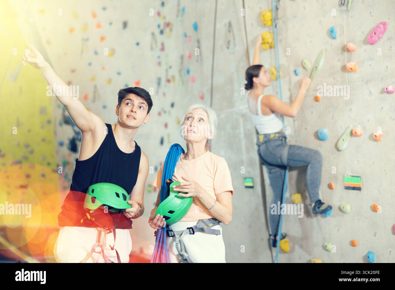 Giovane allenatore maschile che dà istruzioni alla donna anziana sull'arrampicata artificiale parete di roccia di allenamento in palestra di bouldering al coperto Foto Stock