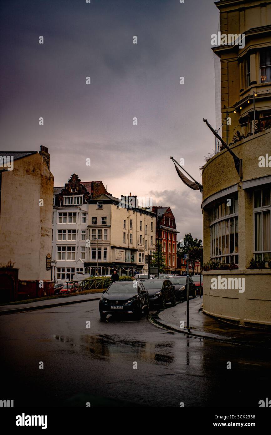 Vista sulla strada con auto parcheggiate su una strada piovosa Foto Stock