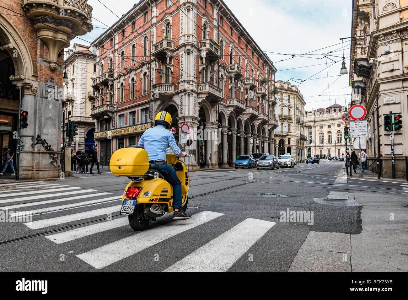 Una foto a livello di strada a Torino, Italia, con una persona su una Vespa gialla brillante in un incrocio. La fotografia mette in risalto il classico sco Foto Stock