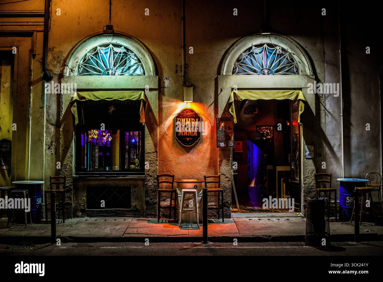 Una scena di strada notturna a Torino, in Italia, incentrata sull'ingresso illuminato di un bar. La fotografia presenta una facciata classica dell'edificio ad arco Foto Stock