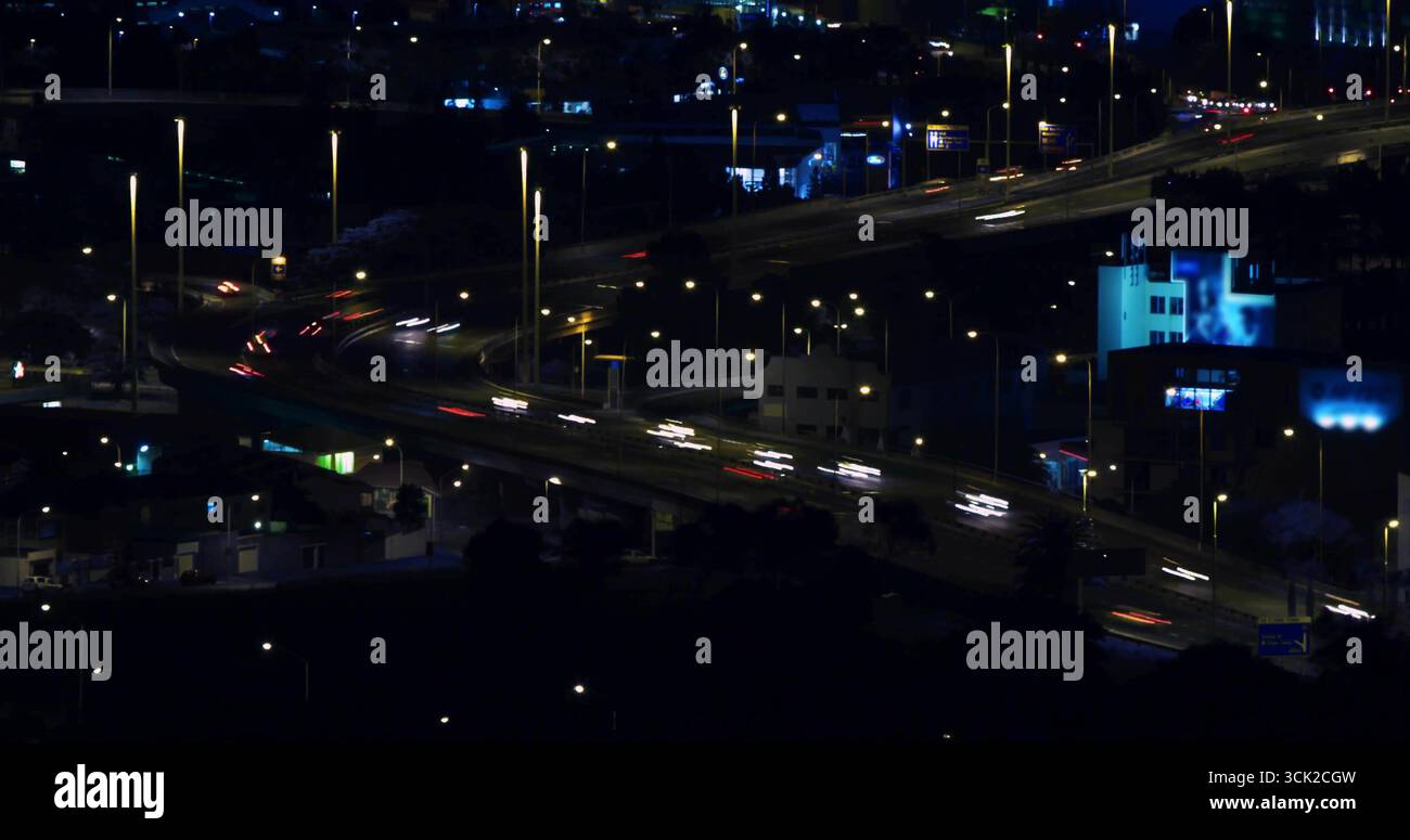 Sorpasso serpeggiante che trasporta veicoli in movimento con percorsi leggeri in città di notte, con segnaletica al neon Foto Stock