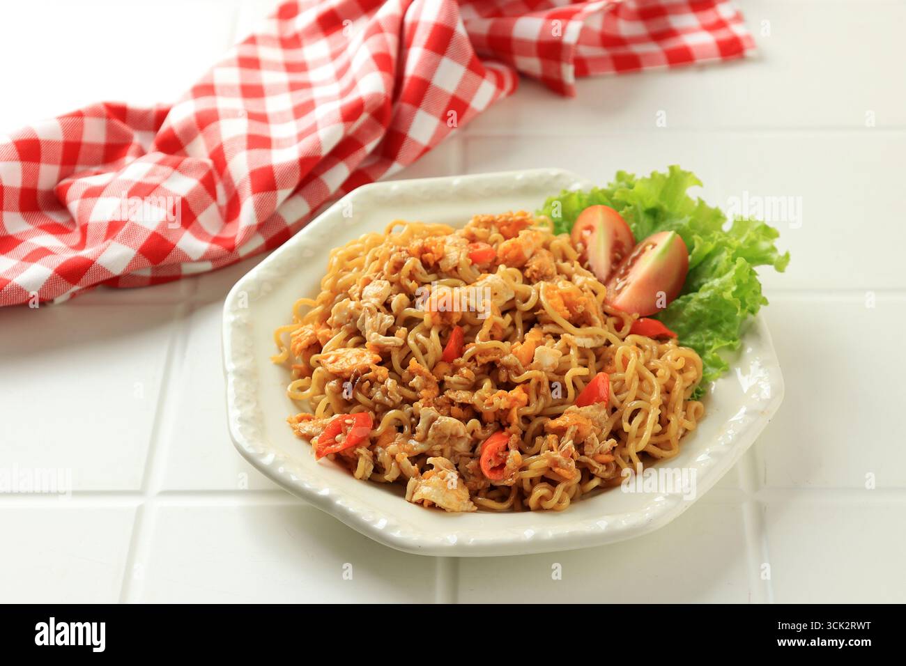Primo piano di piccanti tagliatelle fritte Indomie Goreng Pedas con peperoncino servito su un piatto esagonale crema su un tavolo bianco Foto Stock