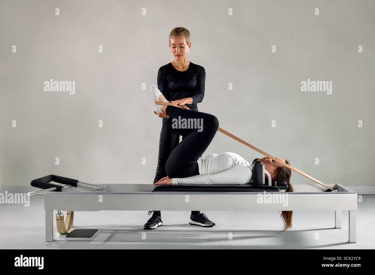 Un istruttore specializzato di Pilates guida un cliente durante una sessione di esercizi riformatori. Questa sessio mette in evidenza movimenti precisi e tecniche di stretching Foto Stock