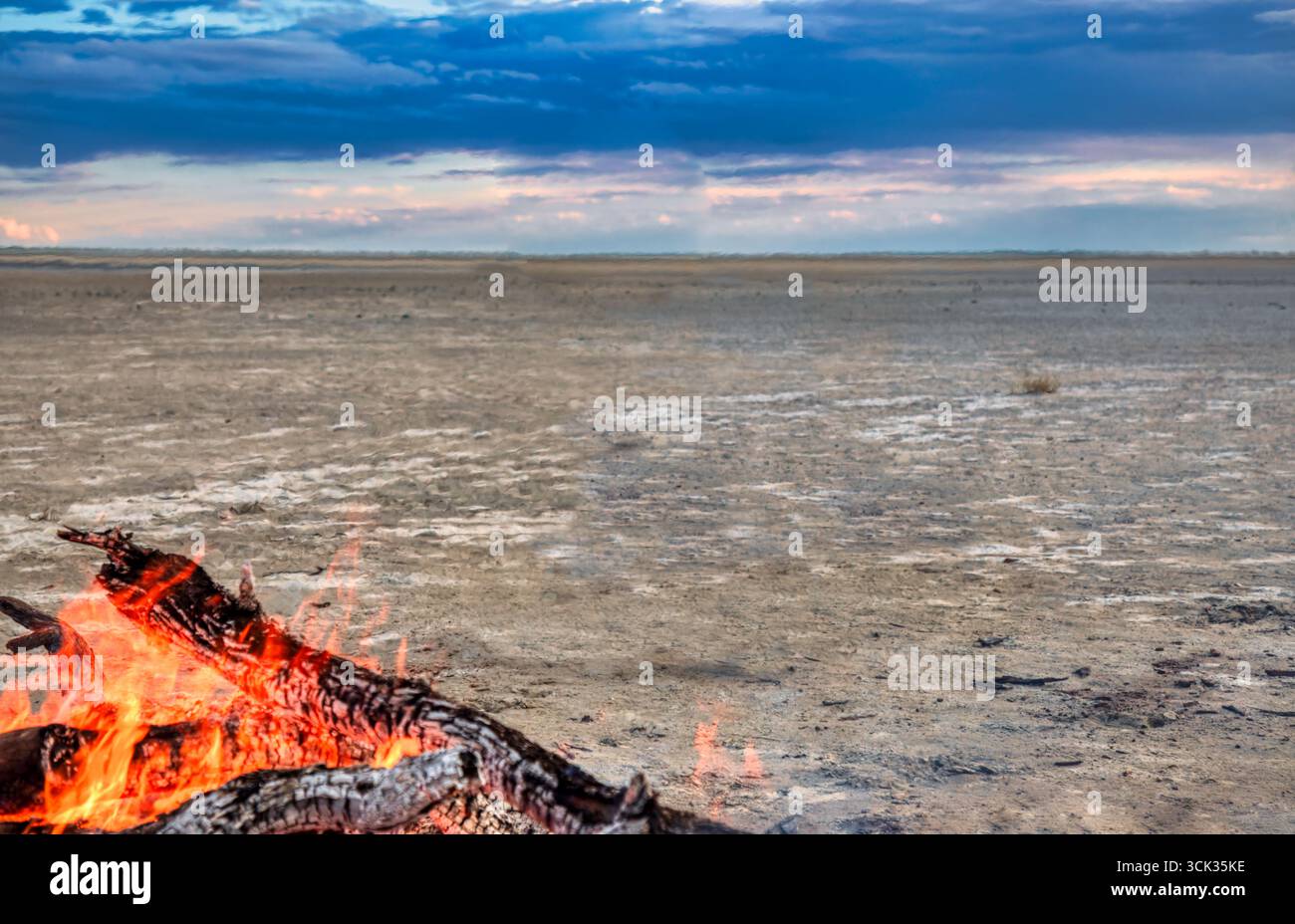 africa turismo, falò con tronchi nel deserto, pianura al tramonto, cielo arancione con nuvole all'orizzonte, solitudine in una regione remota Foto Stock
